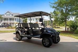 A black golf cart parked on a driveway with a residential house in the background. - The Crabby Buffalo𓇼Golf Cart+Outdoor Oasis+Cozy (Oak Island)