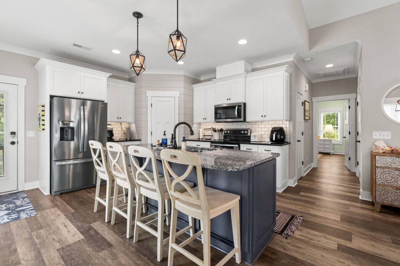A modern kitchen with white cabinetry, stainless steel appliances, and a central island with bar stools.