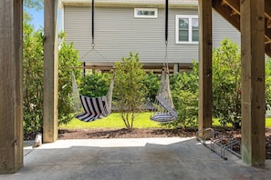 A wooden pergola with two hanging hammocks, a concrete patio, and a house in the background. - The Crabby Buffalo𓇼Golf Cart+Outdoor Oasis+Cozy (Oak Island)