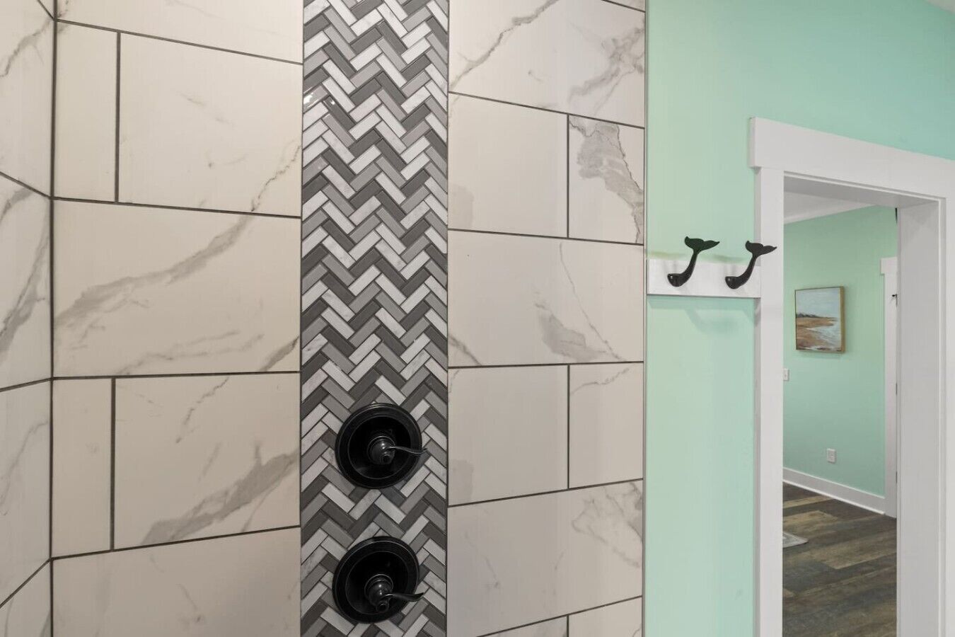 A hallway with a herringbone-patterned wall and a door with two black wall hooks.