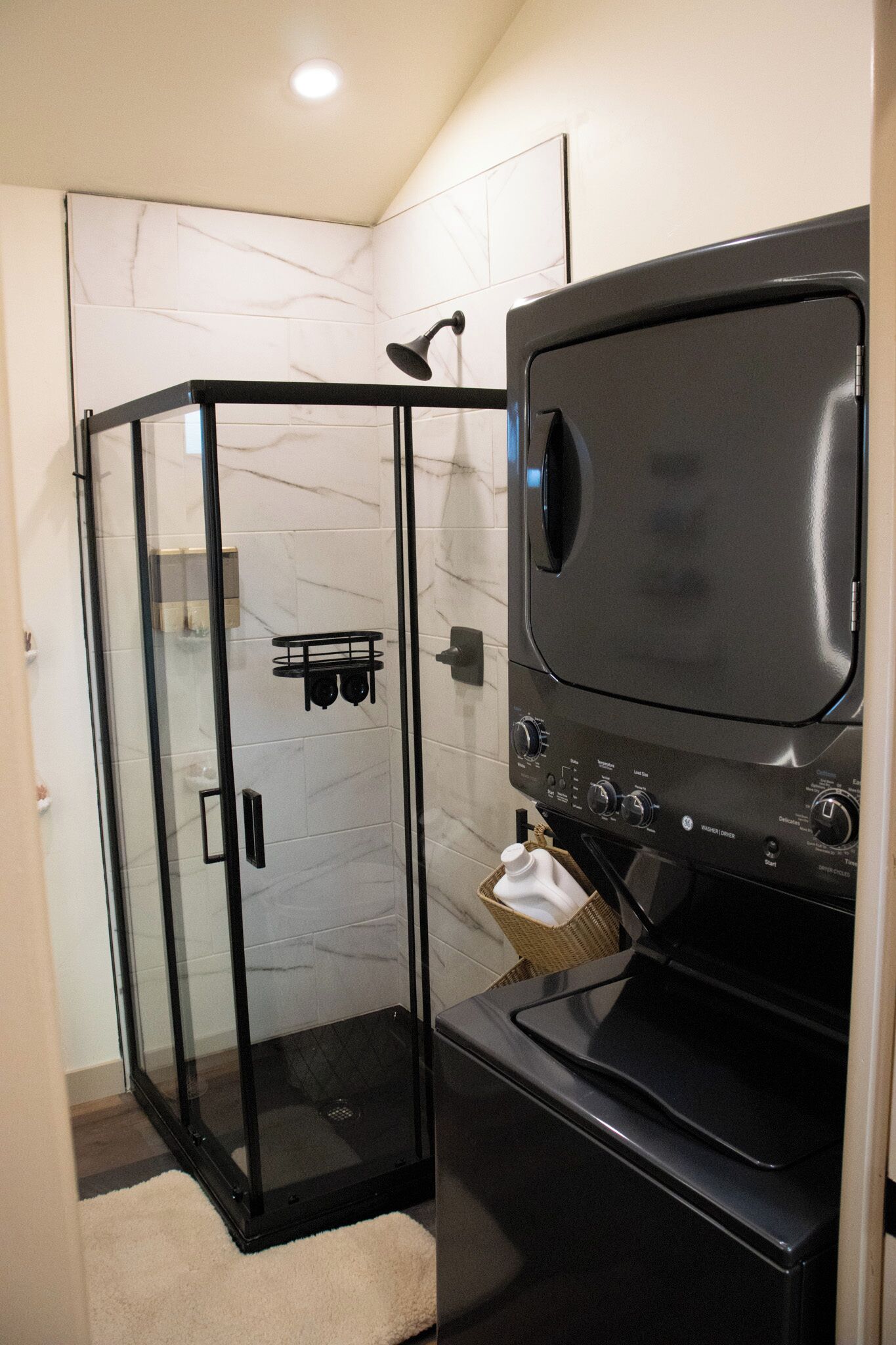 Une salle de bain moderne dotée d’une cabine de douche en verre, d’un lave-linge et d’un sèche-linge intégrés, et d’un mur recouvert de carreaux de marbre.