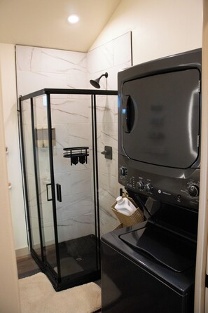 A modern bathroom with a glass shower enclosure, a built-in washer and dryer, and a marble-tiled wall.
