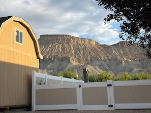 A wooden building with a white fence in front, set against a mountainous backdrop.