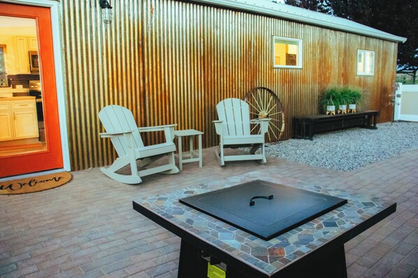 A patio area with two Adirondack chairs, a fire pit, and a wooden building with a corrugated exterior.