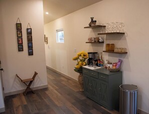 A hallway with a wooden chair, a sink with a vase of sunflowers, and shelves with glassware and bottles.