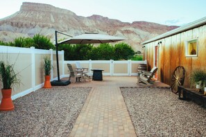 A patio area with a brick pathway, outdoor furniture, and a wooden building with a window.