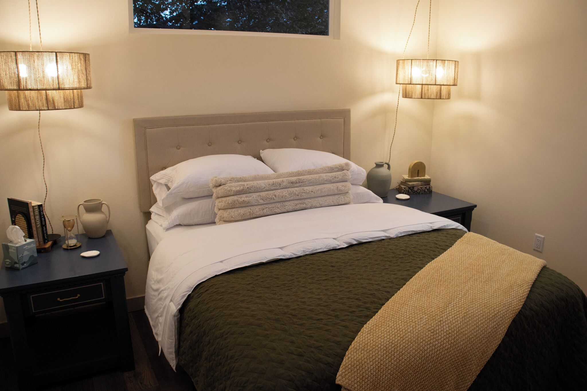 A neatly made bed with a tufted headboard, two bedside tables with lamps, a vase, and a small wooden sculpture.