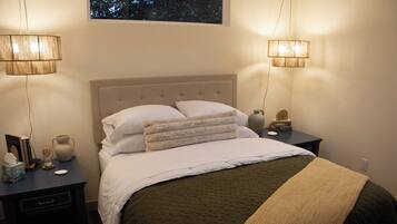 A neatly made bed with a tufted headboard, two bedside tables with lamps, a vase, and a small wooden sculpture.