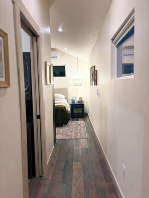 A narrow hallway with a bed, bedside table, and a lamp.