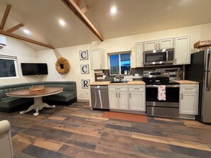 A modern kitchen with white cabinetry, stainless steel appliances, and a wooden dining table.