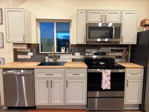A modern kitchen with stainless steel appliances, a wooden countertop, and white cabinetry.