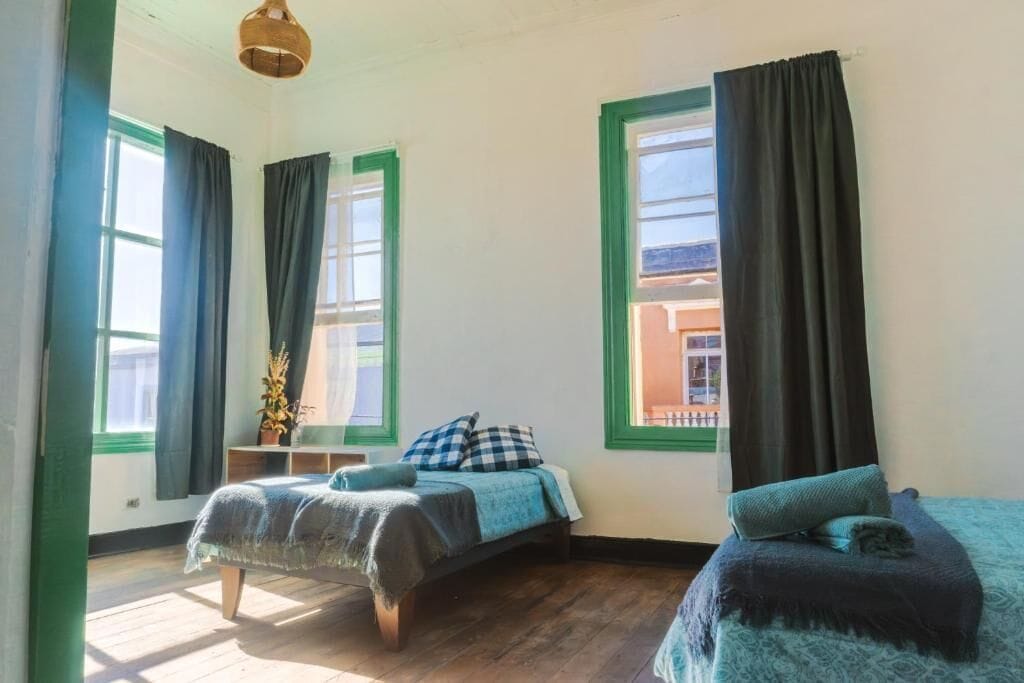 A room with two beds, a small table, and a window with curtains.