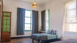 Una habitación con dos camas, piso de madera, un escritorio con silla y una ventana con cortinas.