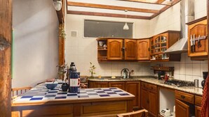 Cuina amb armaris de fusta, taula amb quadres i finestra sobre l'aigüera.