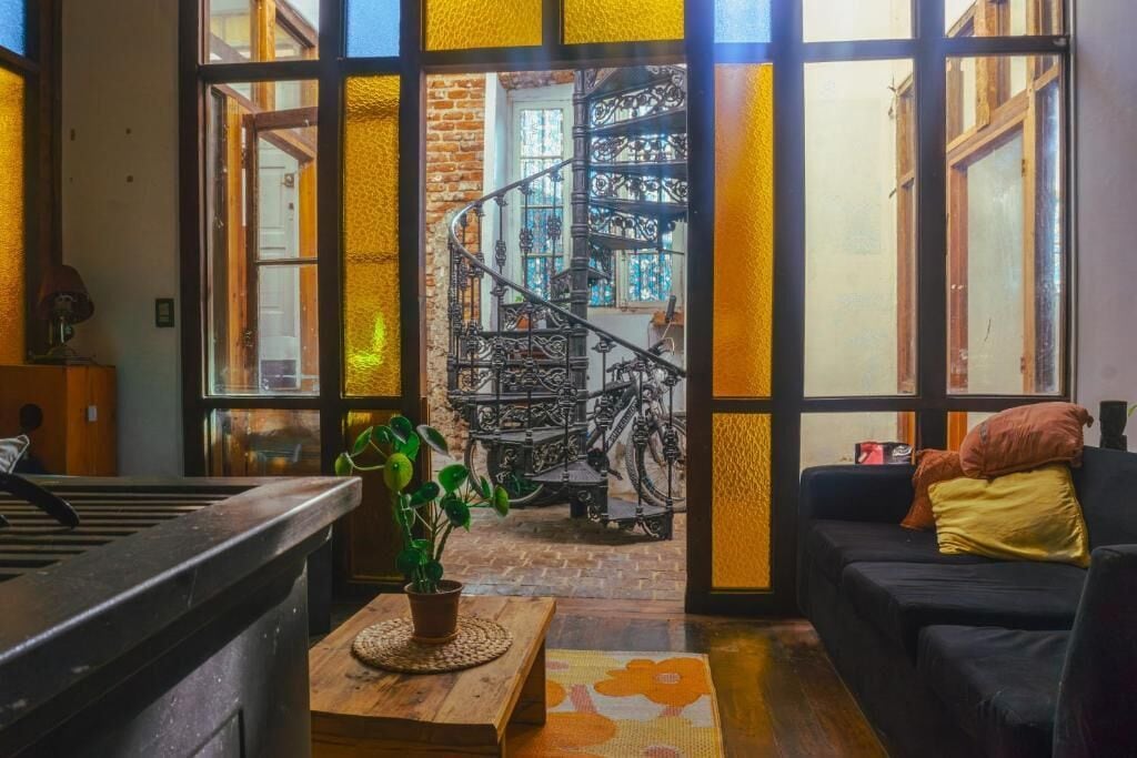 Un intérieur chaleureux avec un escalier menant à un balcon, un canapé noir et une plante en pot.
