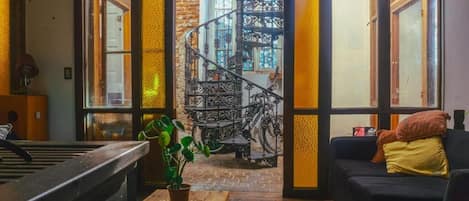 A cozy interior with a staircase leading to a balcony, a black sofa, and a potted plant.