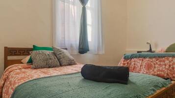 Une chambre avec deux lits, une fenêtre avec des rideaux légers et une petite table avec une lampe.
