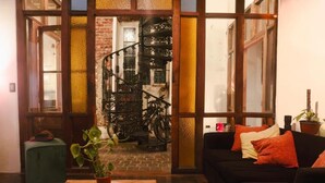 Un espacio de sala acogedor con una escalera, un sofá, una mesa con una planta y vistas a bicicletas al fondo.