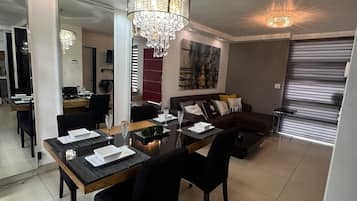 Un espace repas moderne avec une table en verre, des chaises noires et un lustre.