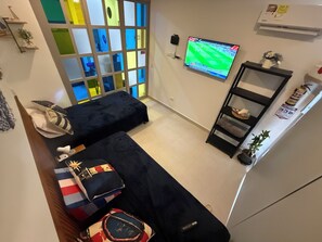 Ein Zimmer mit zwei Betten, einem an der Wand befestigten Fernseher, einem Regal mit Gegenständen und einem Fenster mit Aussicht.
