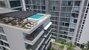 Un edifici modern amb zona de piscina al terrat, múltiples balcons i façana de vidre.