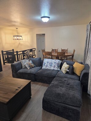 Een woonkamer met een hoekbank, een eettafel met stoelen en een houten salontafel.