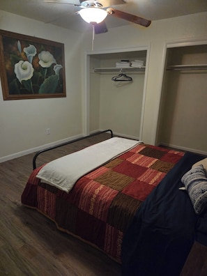 Een slaapkamer met een bed, een plafondventilator, een schilderij en een kledingkast.