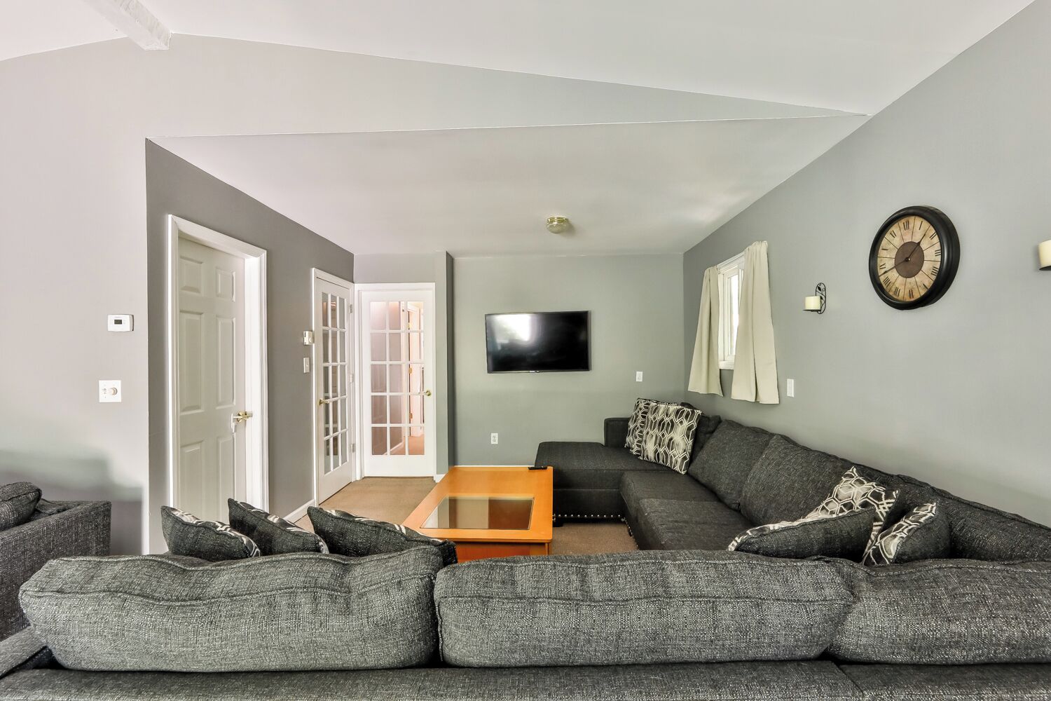 A living room with a sectional sofa, a flat-screen TV, and a door leading to another room.