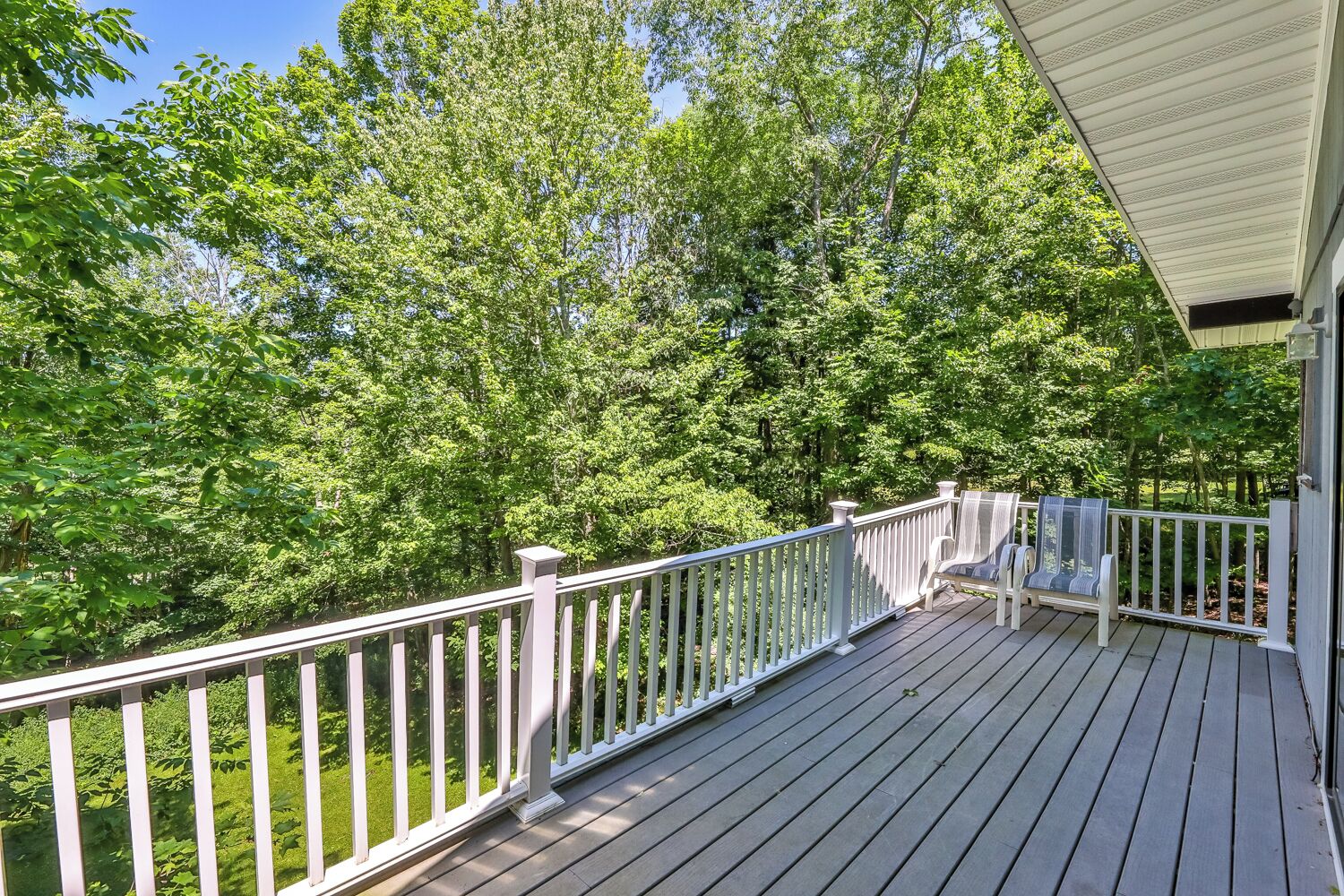 A wooden deck with white railings overlooking a forested area.