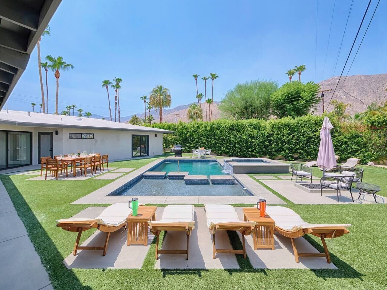 A modern outdoor pool area with lounge chairs, a dining table, and a well-maintained lawn.