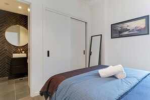 A hotel room with a bed, a bathroom with a herringbone-patterned wall, a round mirror, and a framed picture on the wall. - The Eden Terrace Retreat with Parking and Balcony (Auckland Central)