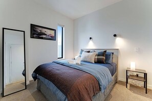 Ein Schlafzimmer mit einem Bett, Nachttischen, einem Fenster und einer Tür.