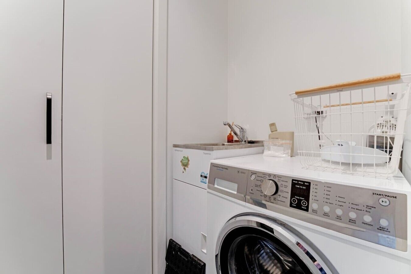 Un espace buanderie compact comprenant un lave-linge à chargement frontal, un étendoir et un petit évier.