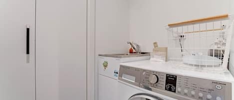 A compact laundry area with a front-loading washing machine, a drying rack, and a small sink.