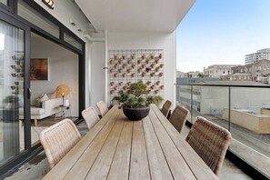 Een balkon met een houten tafel en stoelen, plantenbakken en uitzicht over de stad.