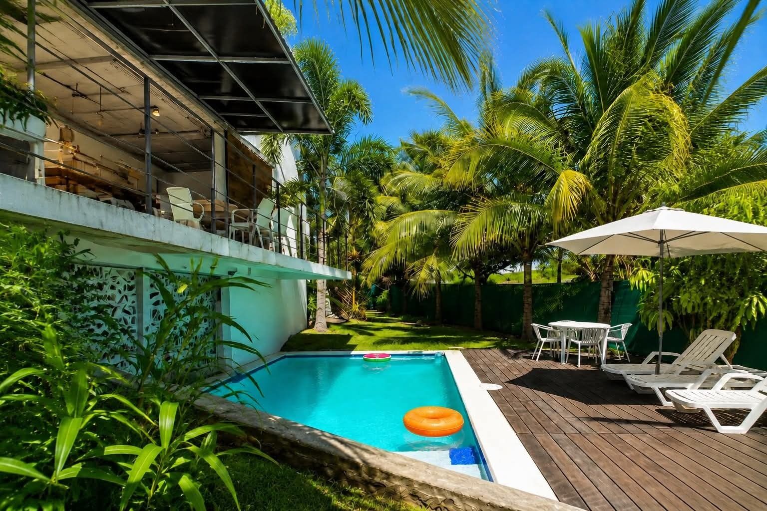 Une piscine avec une terrasse en bois, des chaises longues et un espace de détente extérieur abrité.