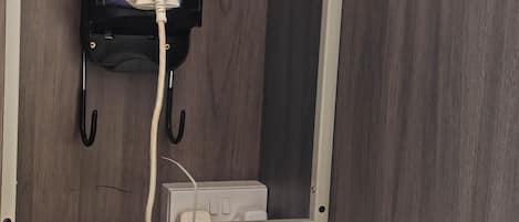 A compact bed with a patterned bedspread, a wall-mounted iron, and a power outlet.