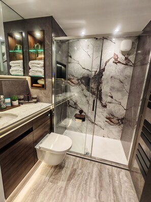 A modern bathroom with a glass-enclosed shower, marble walls, and a vanity with a sink and mirror. - Boutique Luxury Luton | King Bed | Sleeps 4 | Near Airport & Station (Luton)