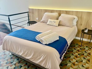 A bed with a blue blanket and a pillow with the text 'enjoy life,' a small table with a lamp, and a geometric patterned floor. - Cozy 1-bedroom 80m2 apartment in Miraflores with pool (Miraflores)