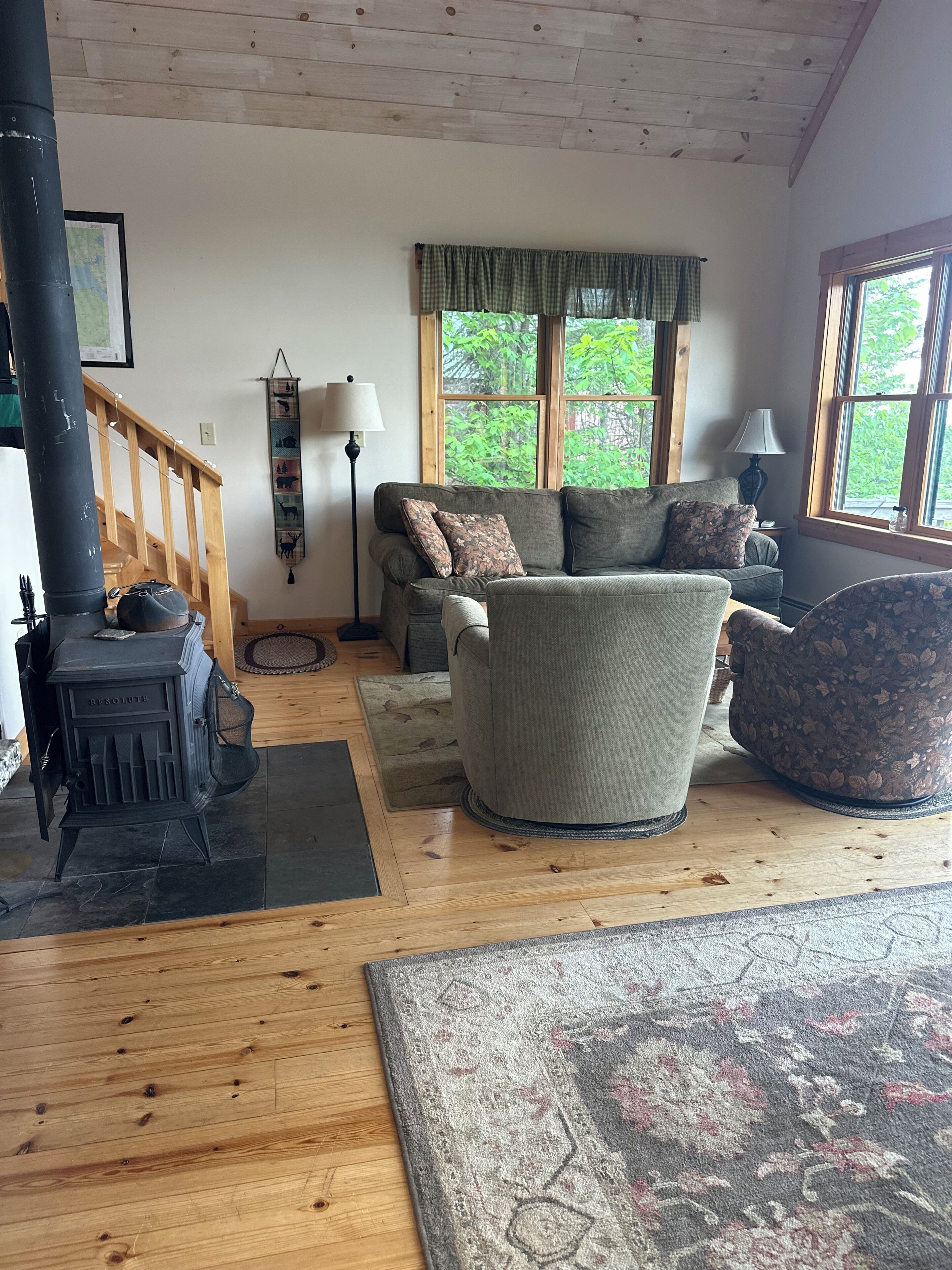 Un salon chaleureux avec une cheminée, un canapé, un tapis à motifs et une vue sur la verdure à l’extérieur.