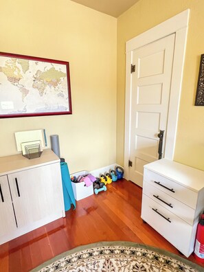A room with a wooden floor, a white cabinet, a white drawer unit, a map on the wall, and a door. - Cozy North Park Home with tranquil patios, AC, located near Balboa Park. (San Diego)