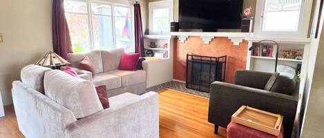 Una sala de estar con sofá, sillón, otoman, chimenea y televisor.