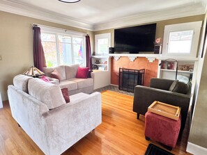 Un salon comprenant un canapé, un fauteuil et un pouf, une cheminée et un téléviseur.