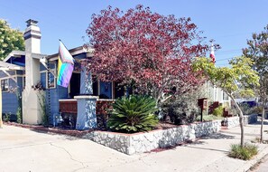 Une maison d’habitation avec un mur de soutènement en pierre, un drapeau et un arbre aux feuilles rouges.