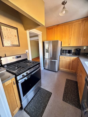 A kitchen with a stainless steel stove, refrigerator, and microwave. There is a wooden cabinet and a countertop. - Cozy North Park Home with tranquil patios, AC, located near Balboa Park. (San Diego)