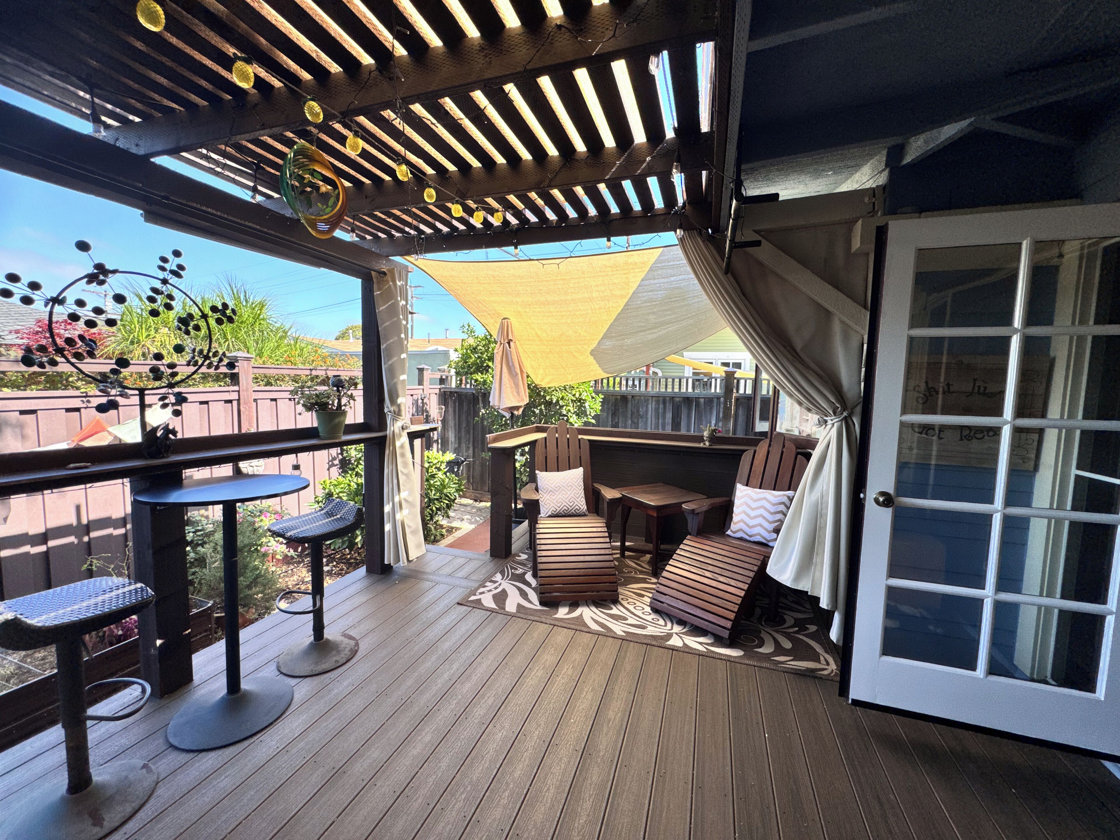 A wooden deck with outdoor seating, a pergola with string lights, and a covered area with a door.