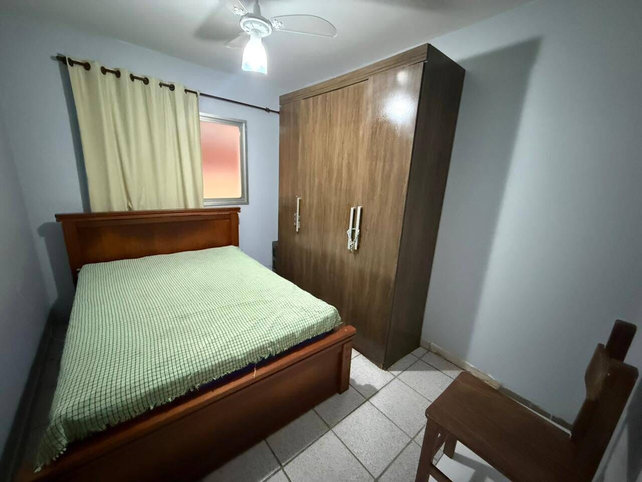 A bedroom with a bed, a wardrobe, a chair, and a ceiling fan.