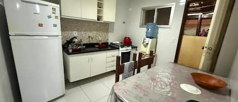 A compact kitchen with white cabinets, a refrigerator, a stove, and a dining table with chairs.