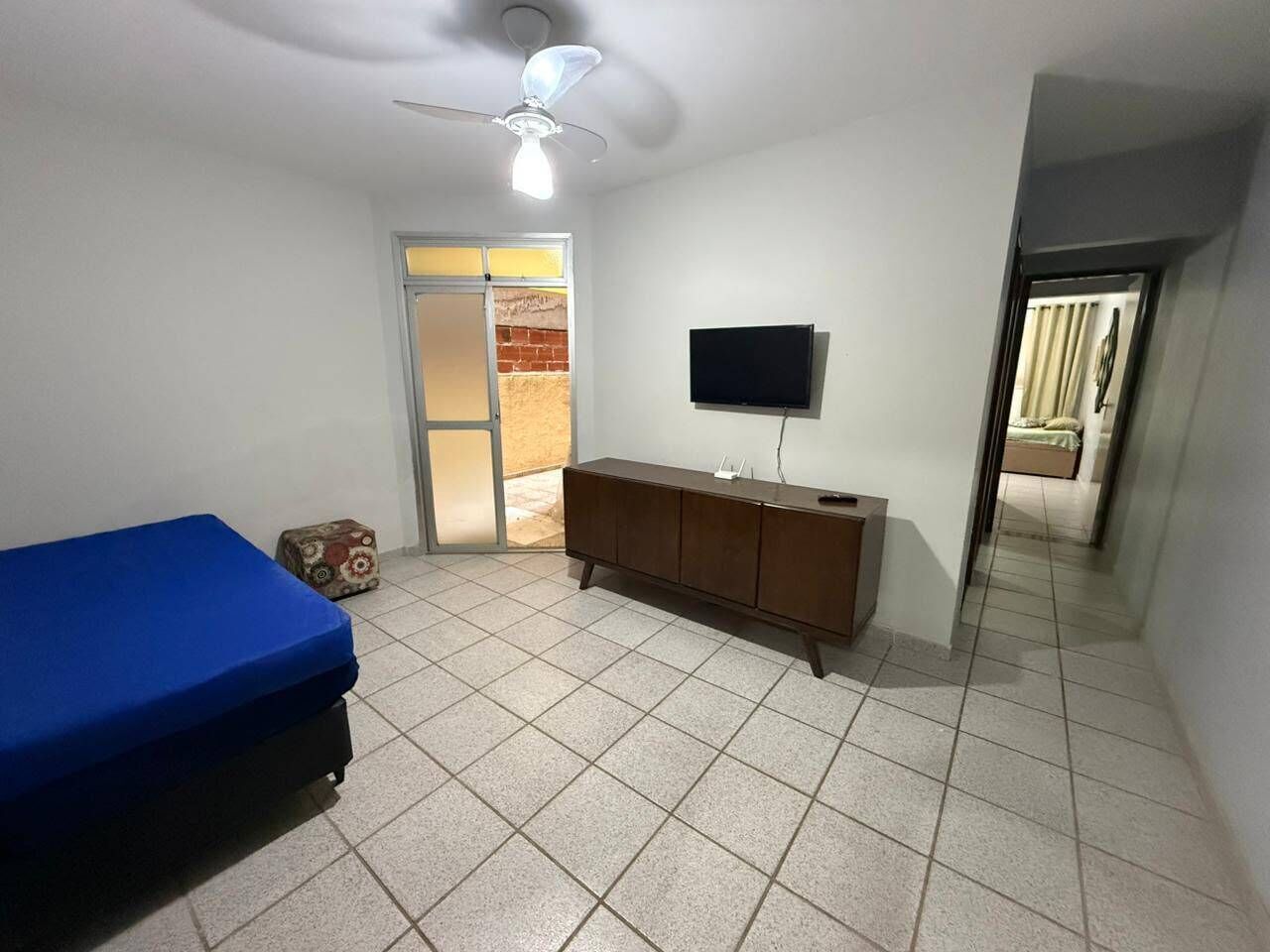 Een kamer met een bed, een aan de muur bevestigde televisie, een plafondventilator en een deur naar een andere kamer.
