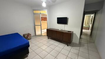 Een kamer met een bed, een aan de muur bevestigde televisie, een plafondventilator en een deur naar een andere kamer.
